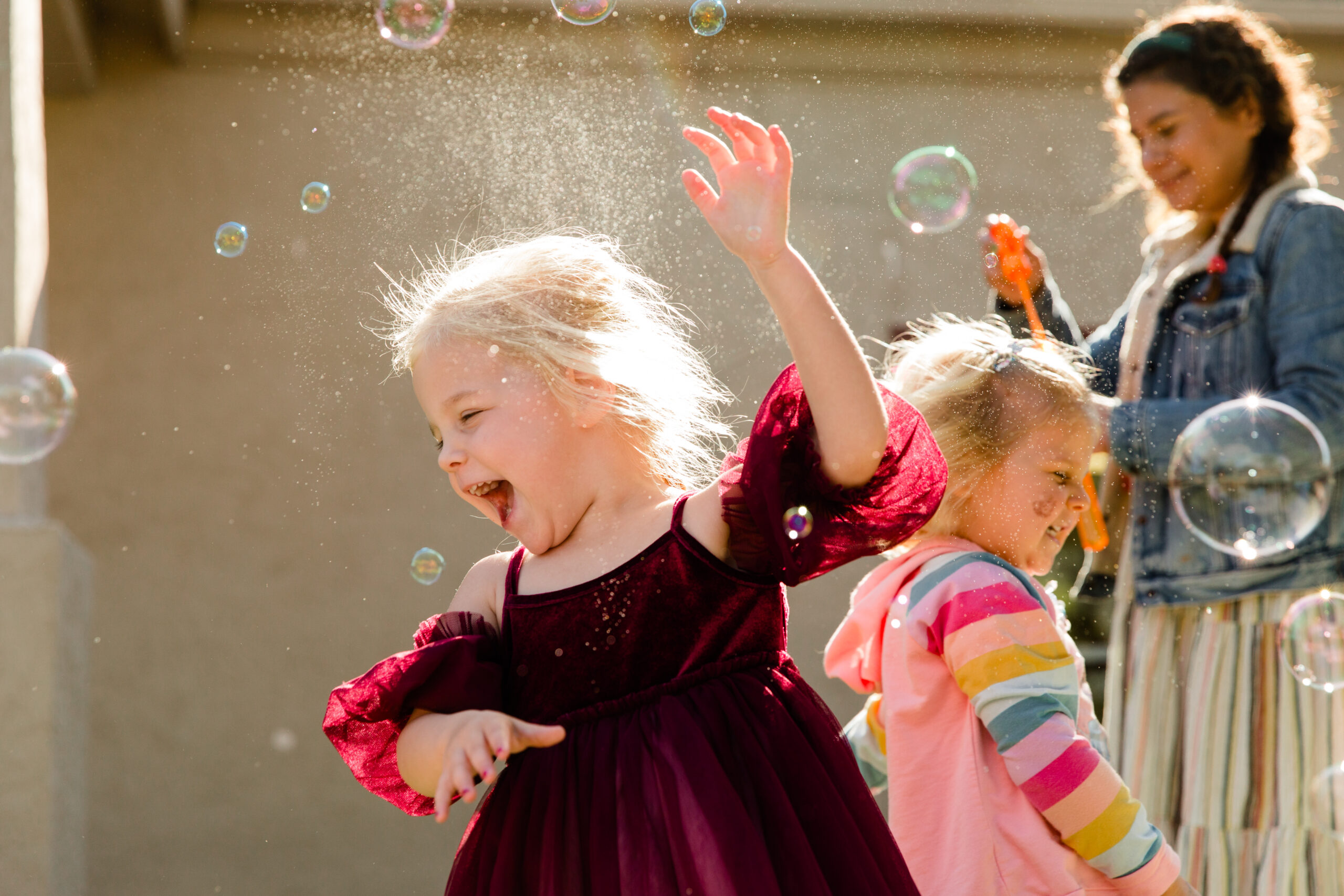 Young girls wearing dresses play outdoors with bubbles.